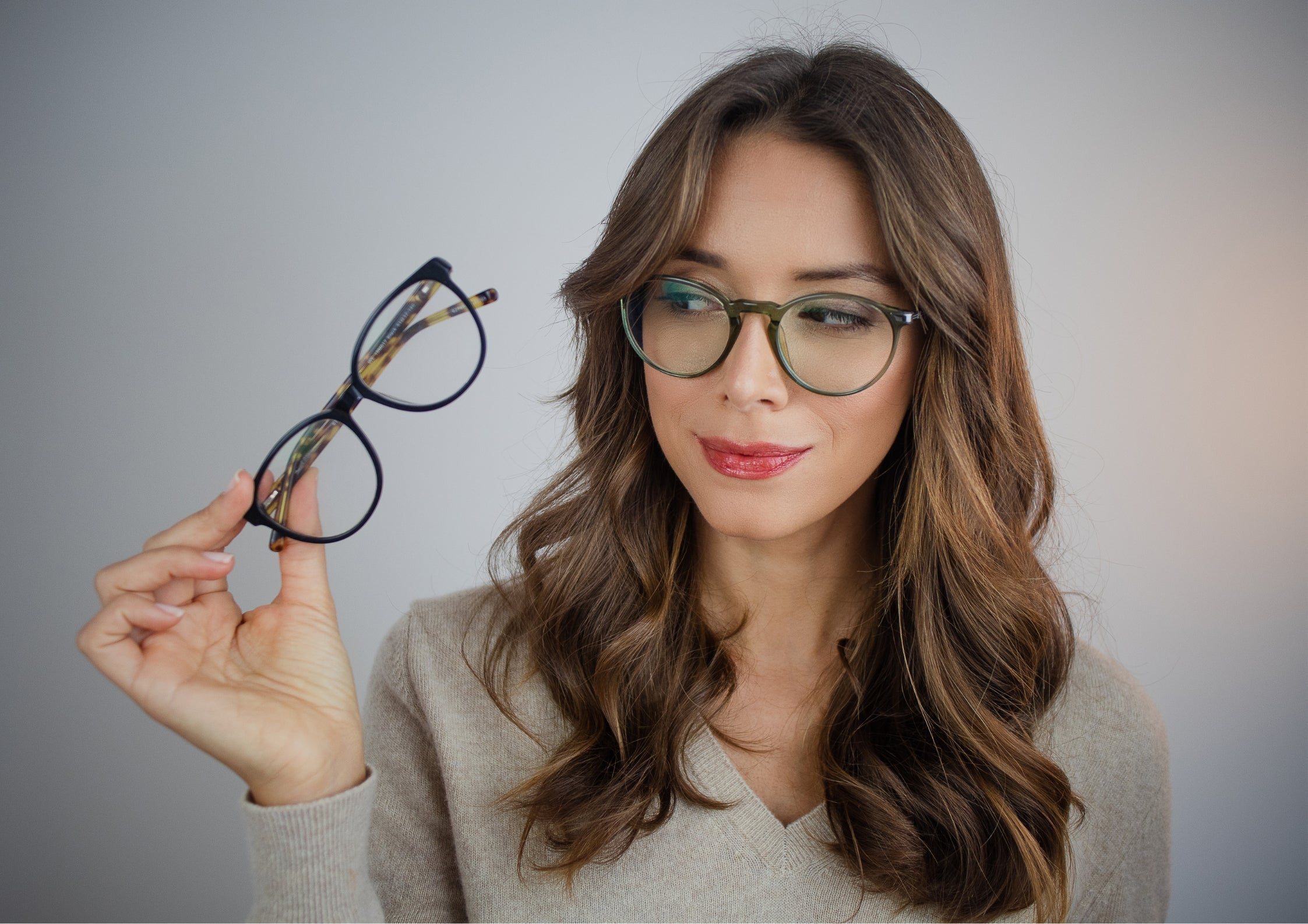 Woman wearing stylish eyeglasses and holding an extra pair, showcasing premium optical eyewear for women.