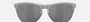 Oakley Frogskins Lite 52 round sunglasses for men in semi-rimless plastic, with grey frame, and prizm black lenses. 63mm in lens size, 10mm in bridge size, and 138mm in temple length.
