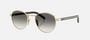 Prada PR B52S ZVN02C round sunglasses for women in full rim steel, with pale gold frame, and grey gradient lenses. 49mm in lens size, 21mm in bridge size, and 145mm in temple length.