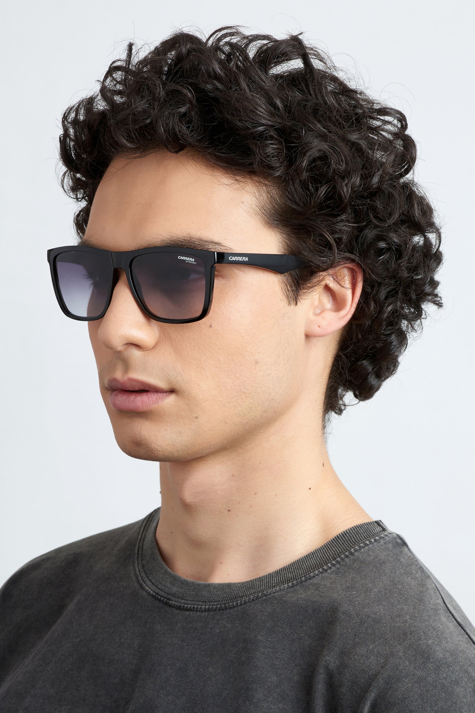 Man wearing black Carrera 5041/S 807 sunglasses and a dark grey shirt against a light grey background facing left side