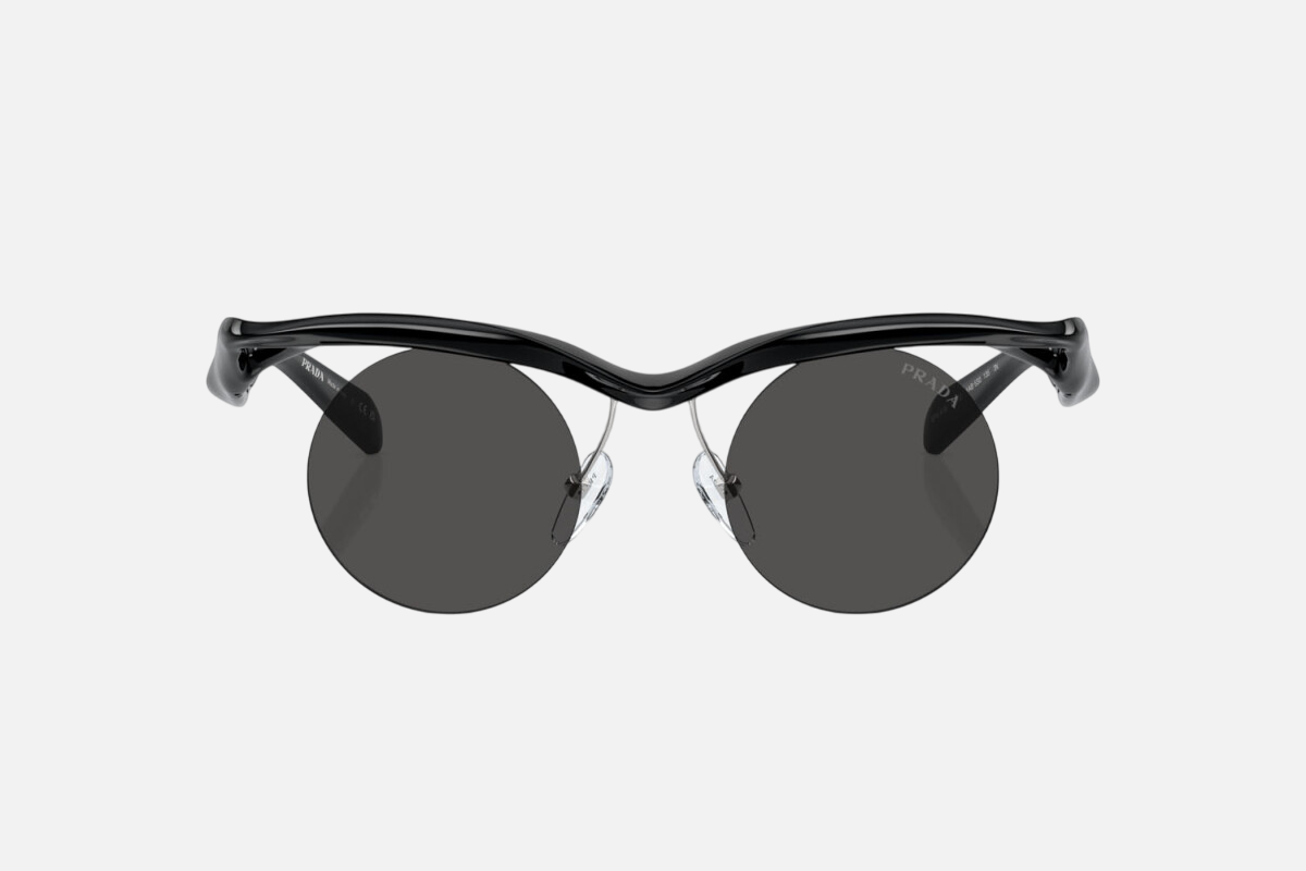 Prada PR A18S 1AB5S0 round sunglasses for men in rimless injected, with black frame, and dark grey lenses. 43mm in lens size, 22mm in bridge size, and 135mm in temple length.